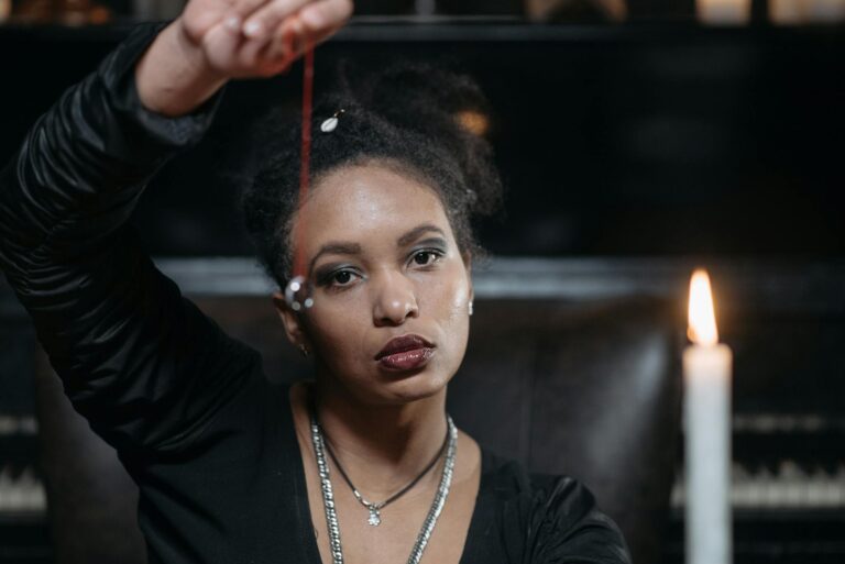 A woman holds a pendulum near a candle, creating a mystical atmosphere.