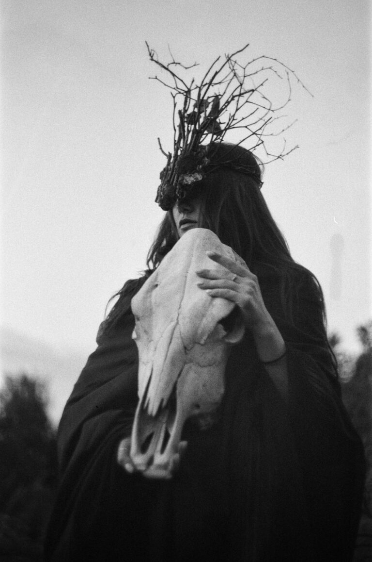 Black and white portrait of a woman holding an animal skull, evoking a mystical and fantasy theme.